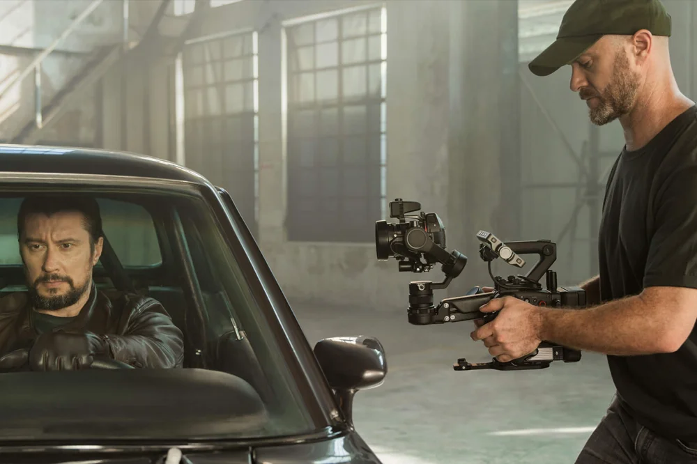 Filmmaker using a DJI Ronin 4D 6K camera rig to film a car scene on set, showcasing real-time stabilisation in action