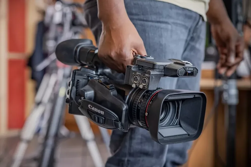 Close-up of Canon XF605 camcorder being held by the handle in a production environment