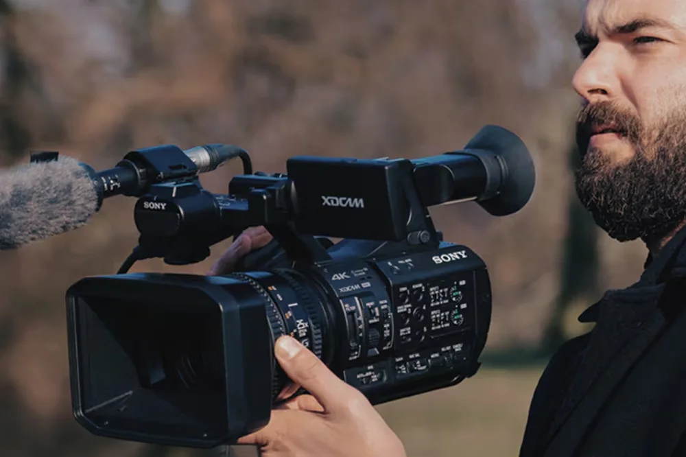 Videographer using Sony PXW-Z190 camcorder with external shotgun microphone during outdoor shoot