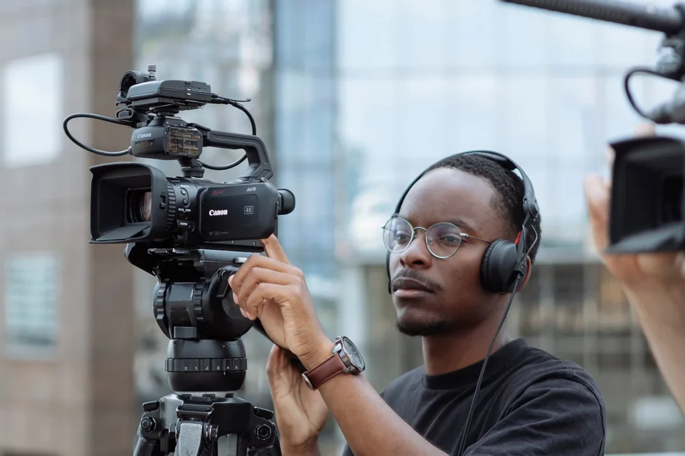 Person operating a Canon handheld camcorder on a tripod with headphones during an outdoor interview